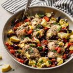 Skillet filled with Greek chicken with olives, tomatoes, and artichokes.