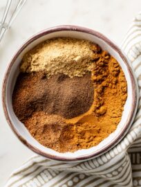 Cinnamon, ginger, nutmeg, cloves, and allspice in a small white bowl.