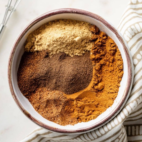 Cinnamon, ginger, nutmeg, cloves, and allspice in a small white bowl.