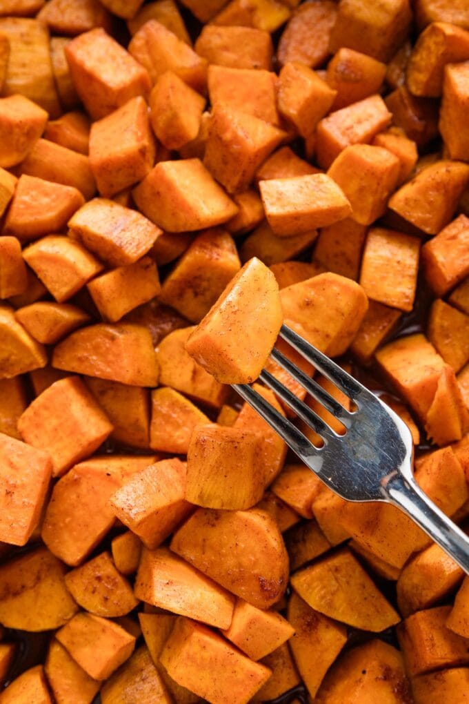 Close up of a fork piercing a cube of sweet potato to show it's tender all the way through.