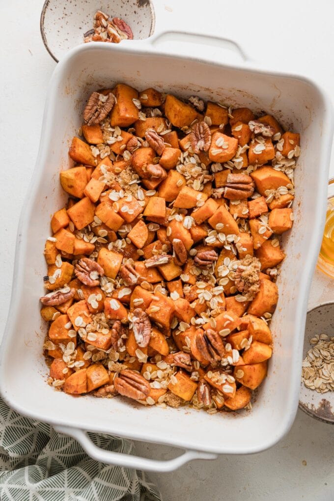 Large baking pan full of chopped sweet potatoes baked in cinnamon honey butter and topped with a light layer of oats, pecans, and brown sugar.