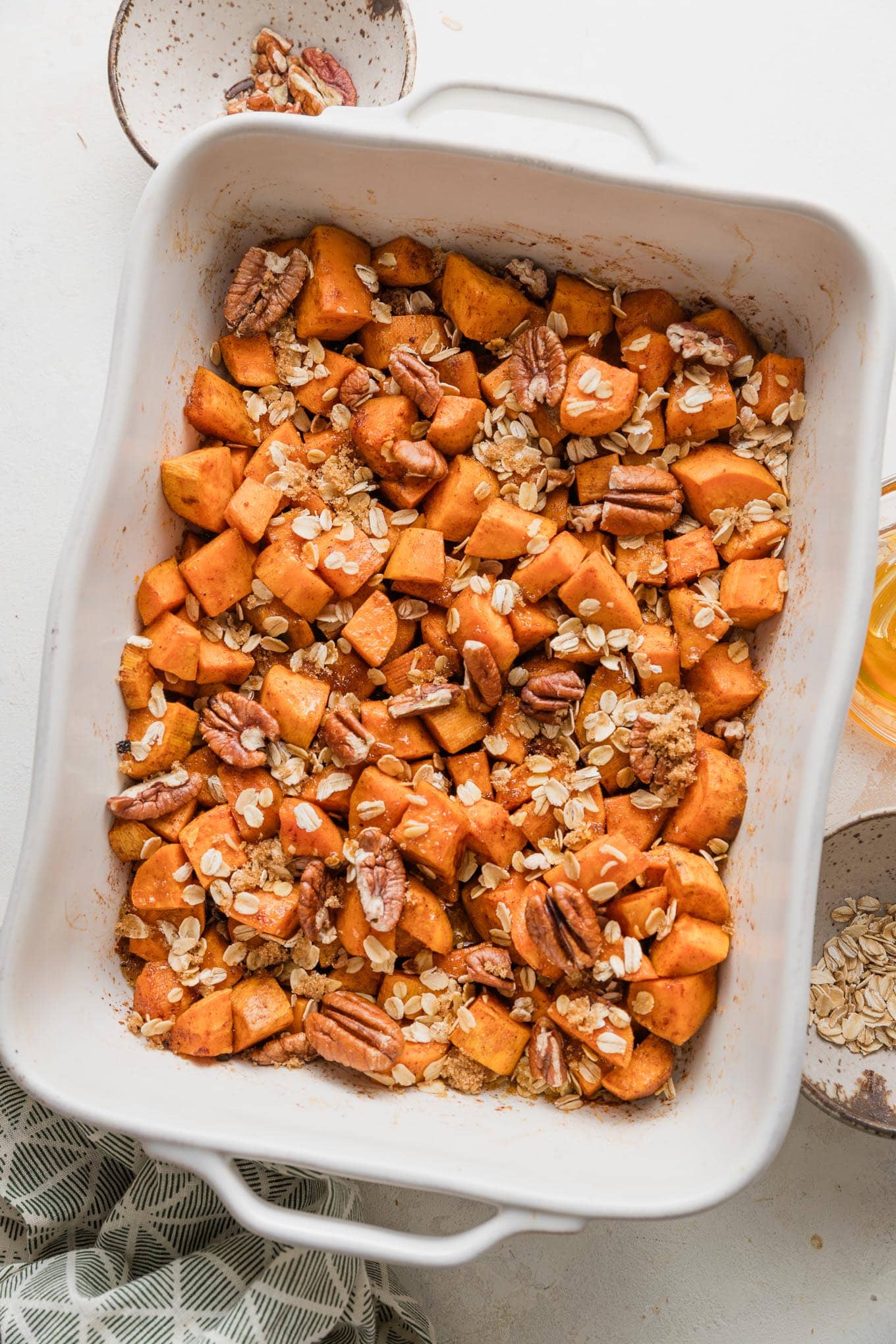 Large baking pan full of chopped sweet potatoes baked in cinnamon honey butter and topped with a light layer of oats, pecans, and brown sugar.