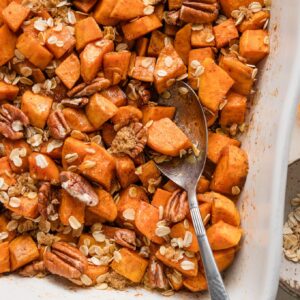 Close up of a serving spoon dipped into a dish of cinnamon honey butter baked sweet potatoes.