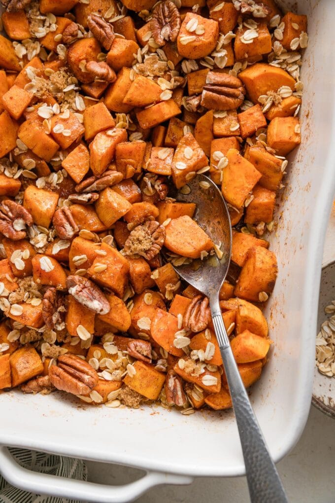 Close up of a serving spoon dipped into a dish of cinnamon honey butter baked sweet potatoes.