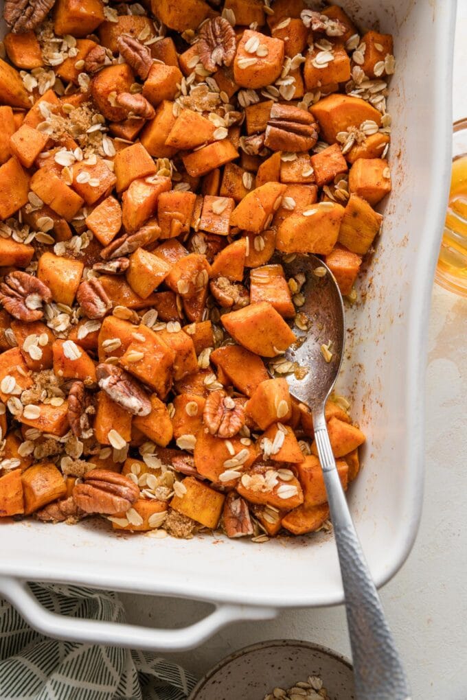 Pan of cubed sweet potatoes baked in a honey butter cinnamon mixture and topped lightly with oats and pecans.