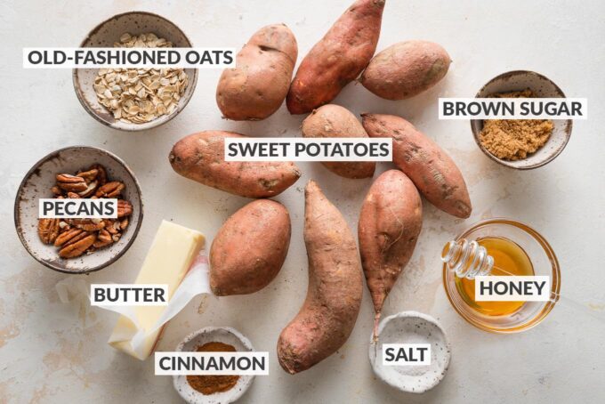 Labeled overhead image of sweet potatoes, butter, honey, cinnamon, salt, old-fashioned oats, pecans, and brown sugar, all in prep bowls and ready to cook.