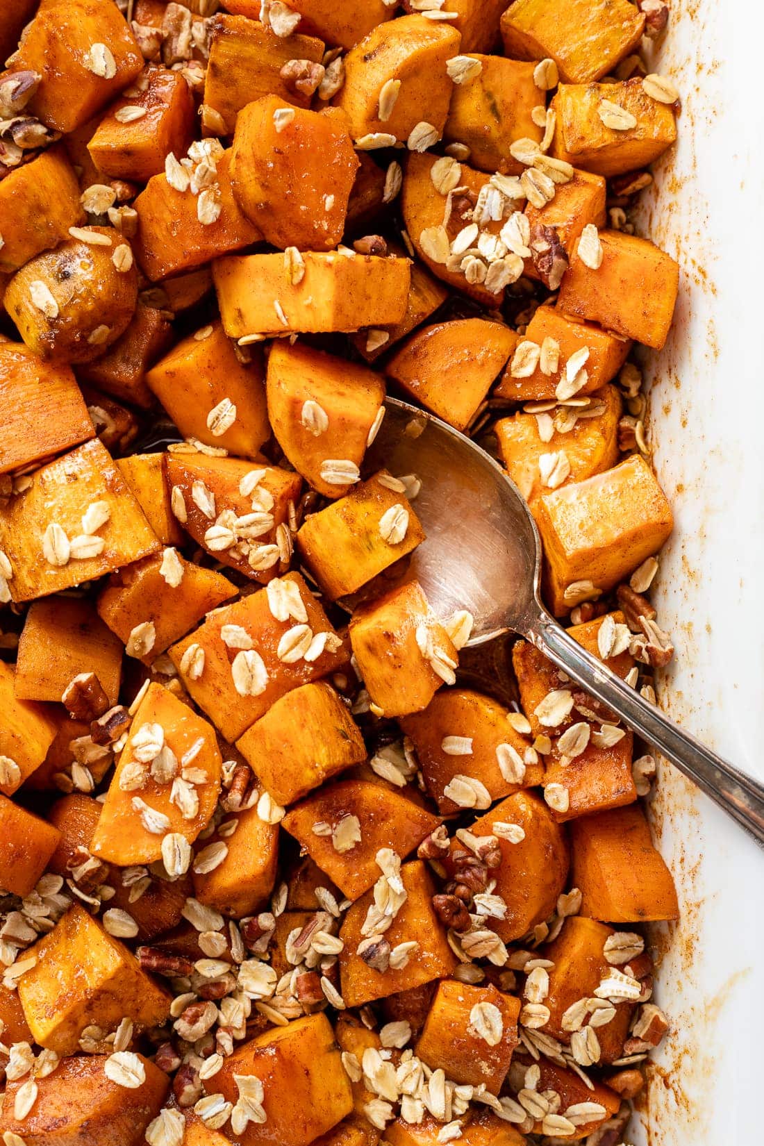 Close up of a spoon serving baked sweet potatoes with oat pecan topping.