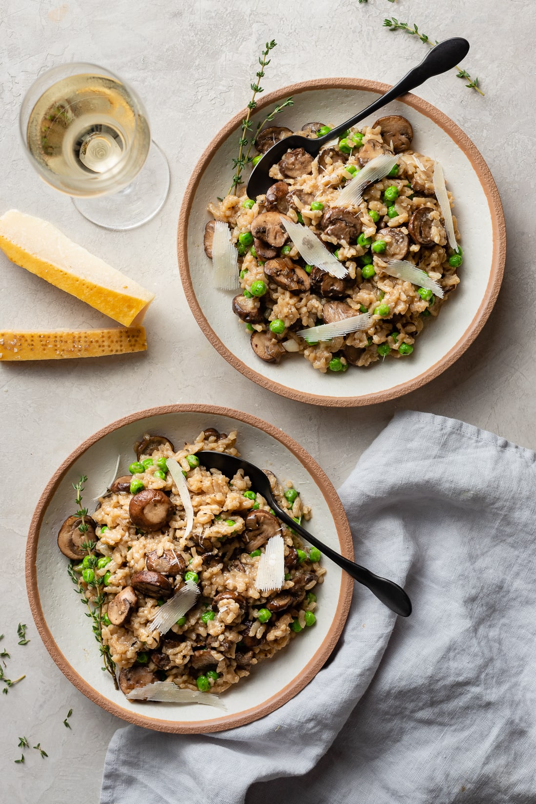 Two bowls of Instant Pot mushroom risotto, a glass of white wine, and Parmesan rinds on the table.