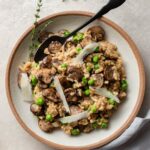 A bowl of mushroom risotto made in the Instant Pot with peas, Parmesan, and a garnish of fresh thyme.