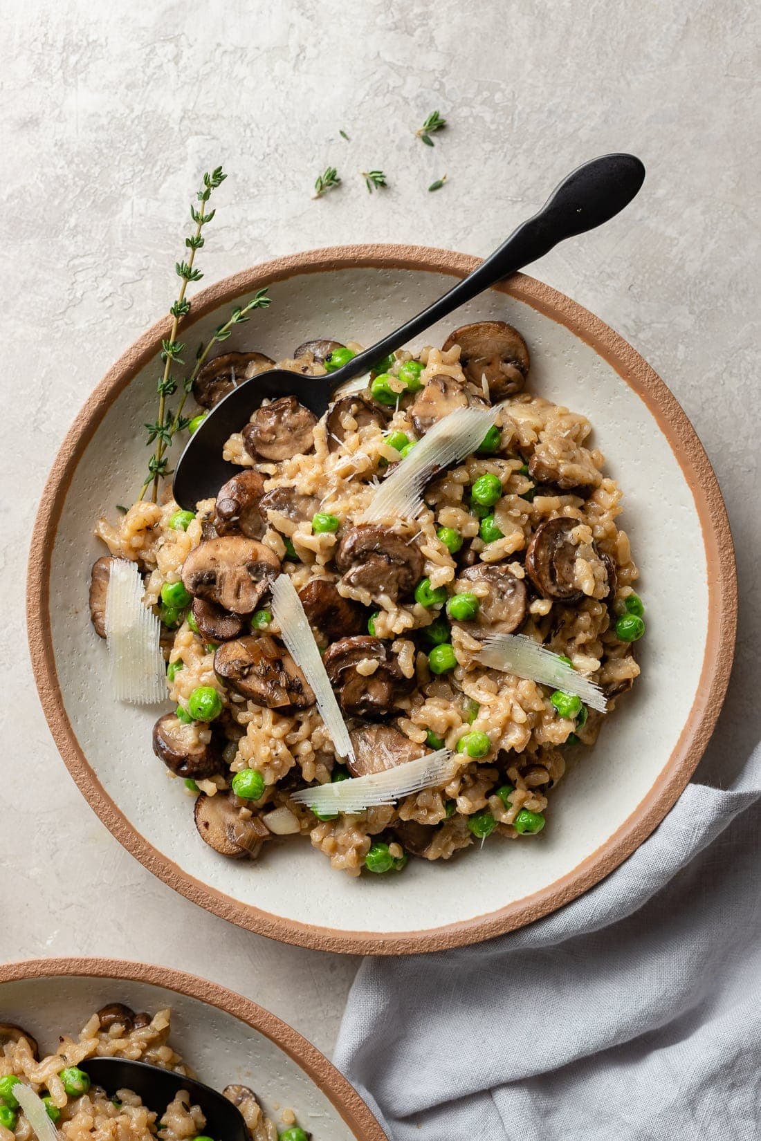 A bowl of mushroom risotto made in the Instant Pot with peas, Parmesan, and a garnish of fresh thyme.