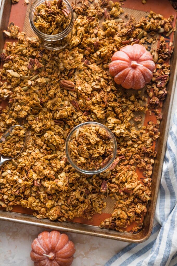 Sheet pan full of just-baked maple pumpkin granola, partially scooped into small jars.