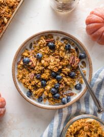Small bowl filled with almond milk, pumpkin granola, and blueberries.