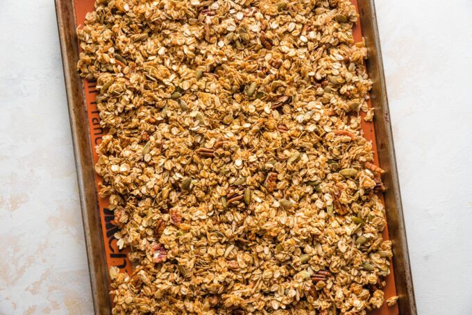 Unbaked pumpkin granola spread out across a rimmed baking sheet.