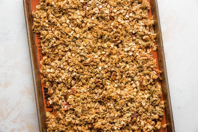 Unbaked pumpkin granola spread out across a rimmed baking sheet.