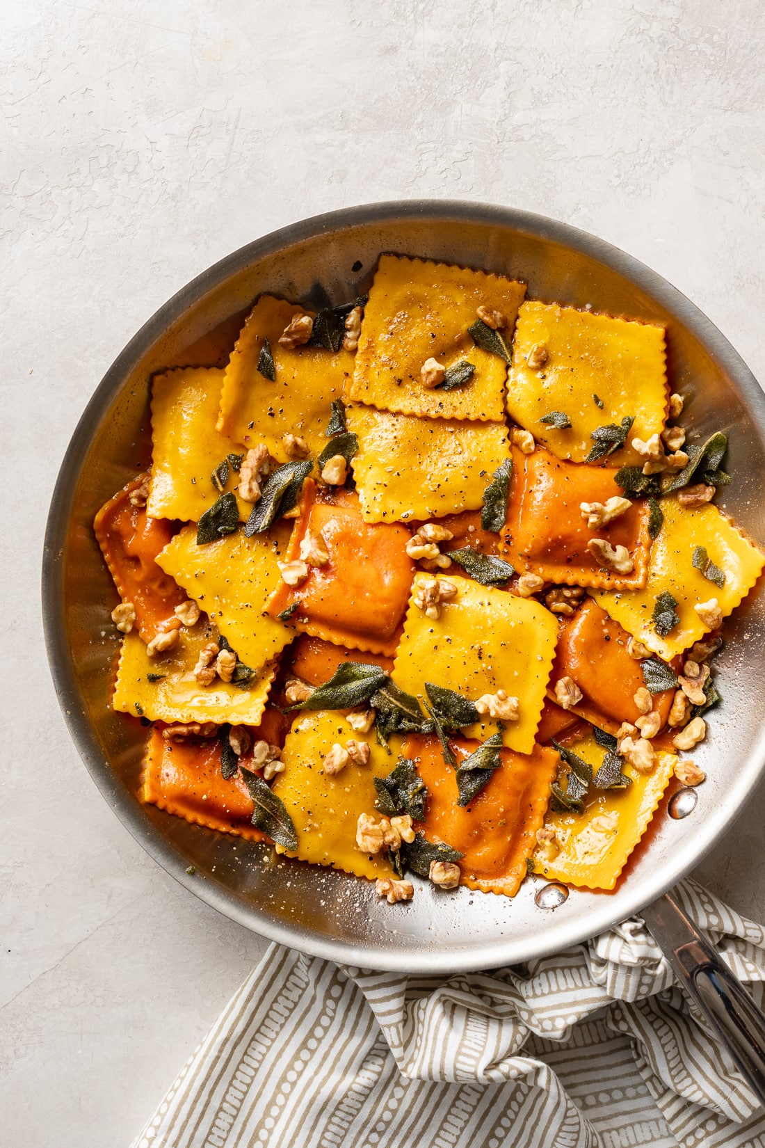 Skillet filled with pumpkin ravioli, sage brown butter sauce, crisped sage leaves, and walnuts.