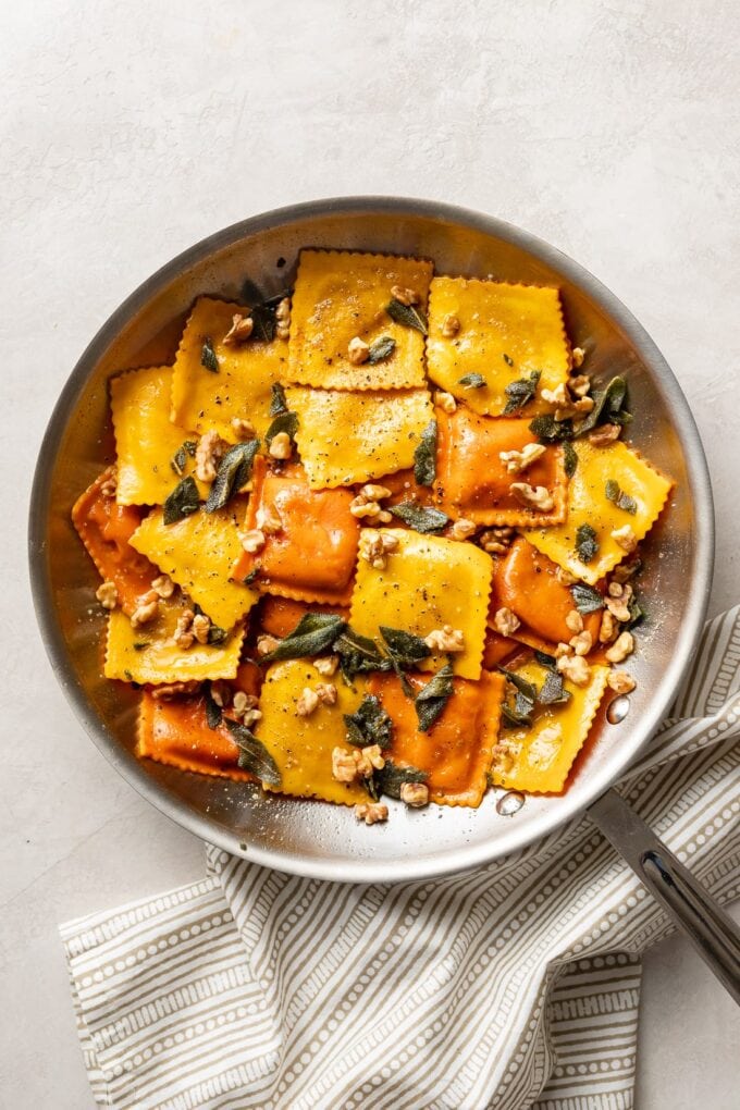 Skillet filled with pumpkin ravioli, sage brown butter sauce, crisped sage leaves, and walnuts.