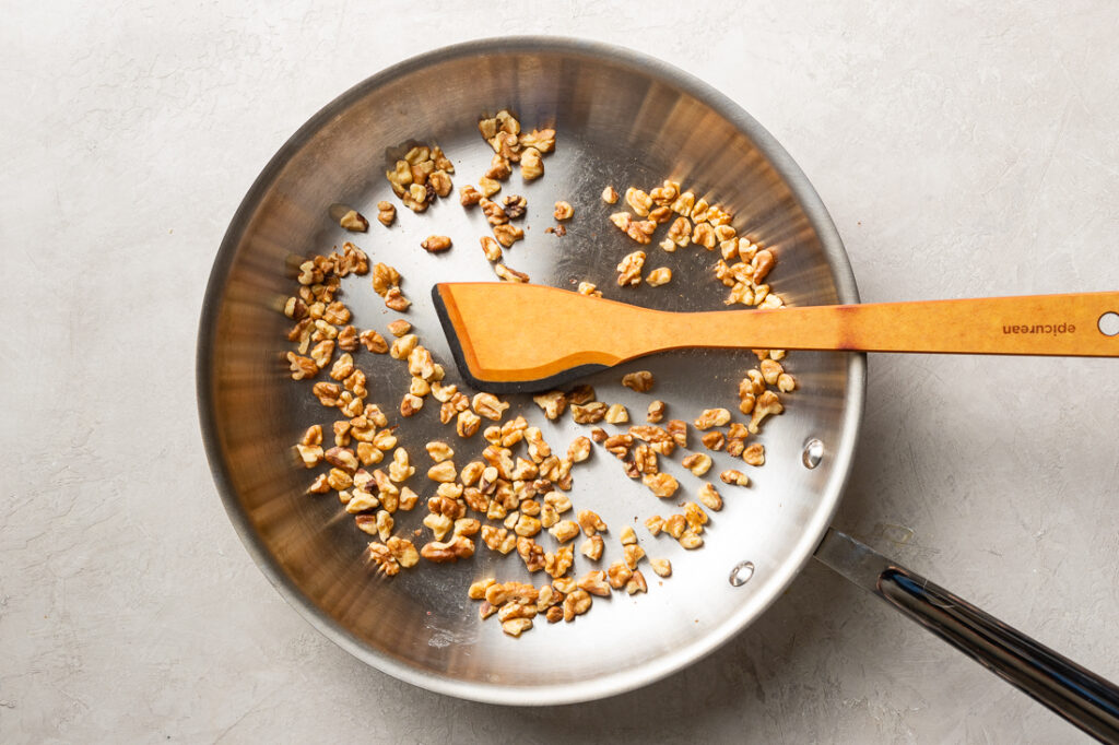 A small handful of walnuts toasting in a large skillet.