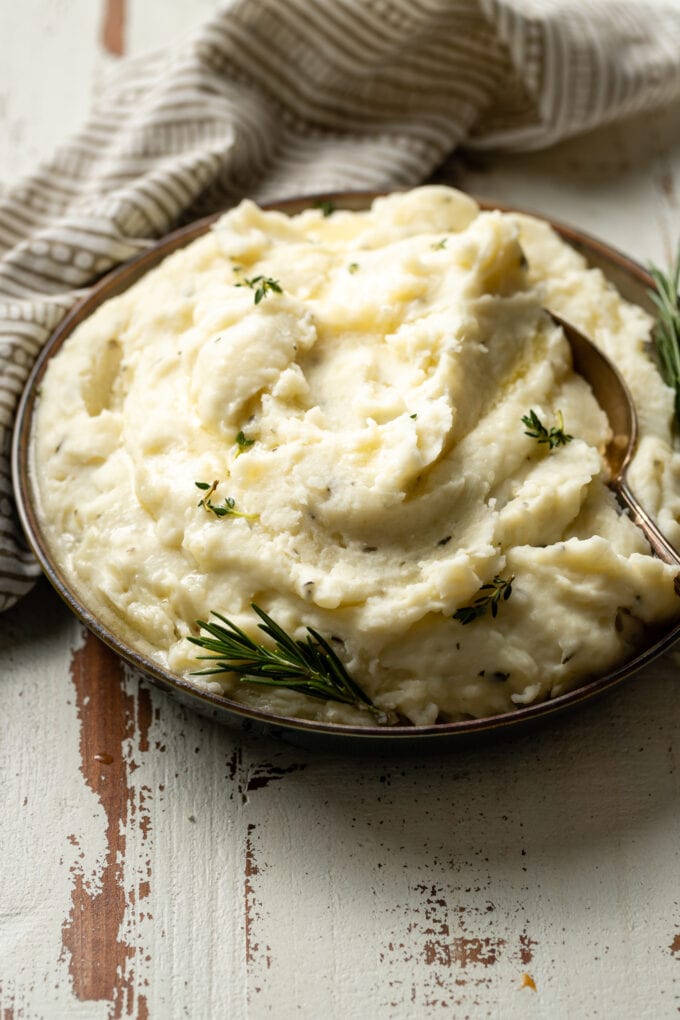 A bowl of fluffy garlic and herb mashed potatoes garnished with fresh rosemary and melted butter.