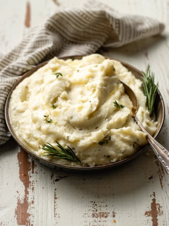A bowl of fluffy garlic and herb mashed potatoes garnished with fresh rosemary and melted butter.