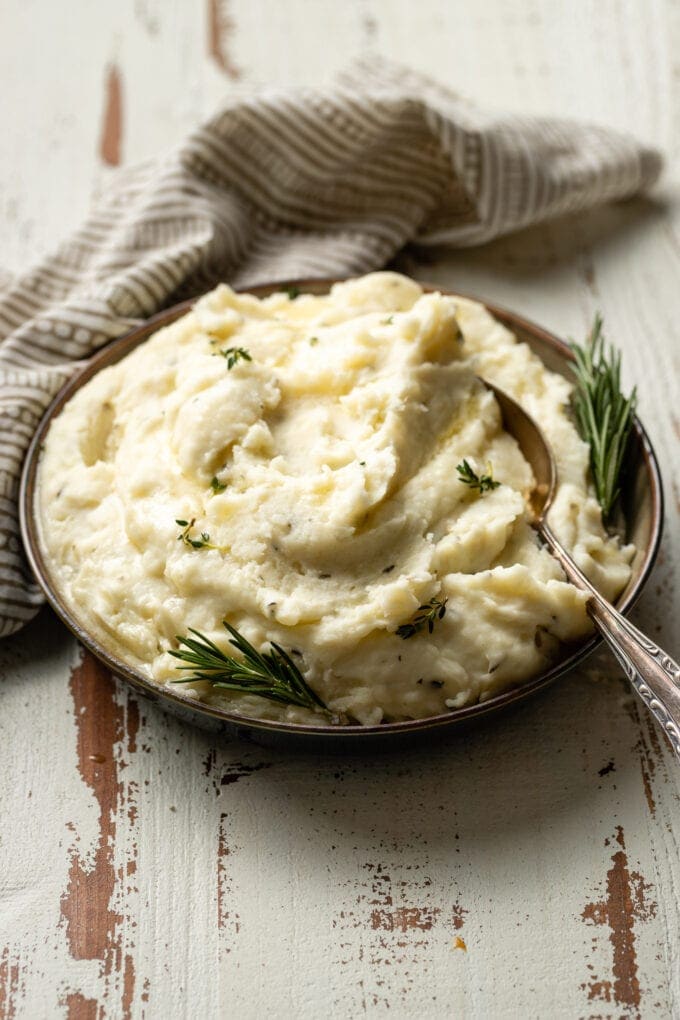 A bowl of fluffy garlic and herb mashed potatoes garnished with fresh rosemary and melted butter.