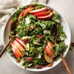 A large bowl of salad with kale, apples, Pecorino cheese, pomegranate seeds, and glazed pecans.