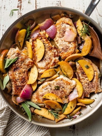 A spoon about to serve helpings of pork chops with apples and onions.