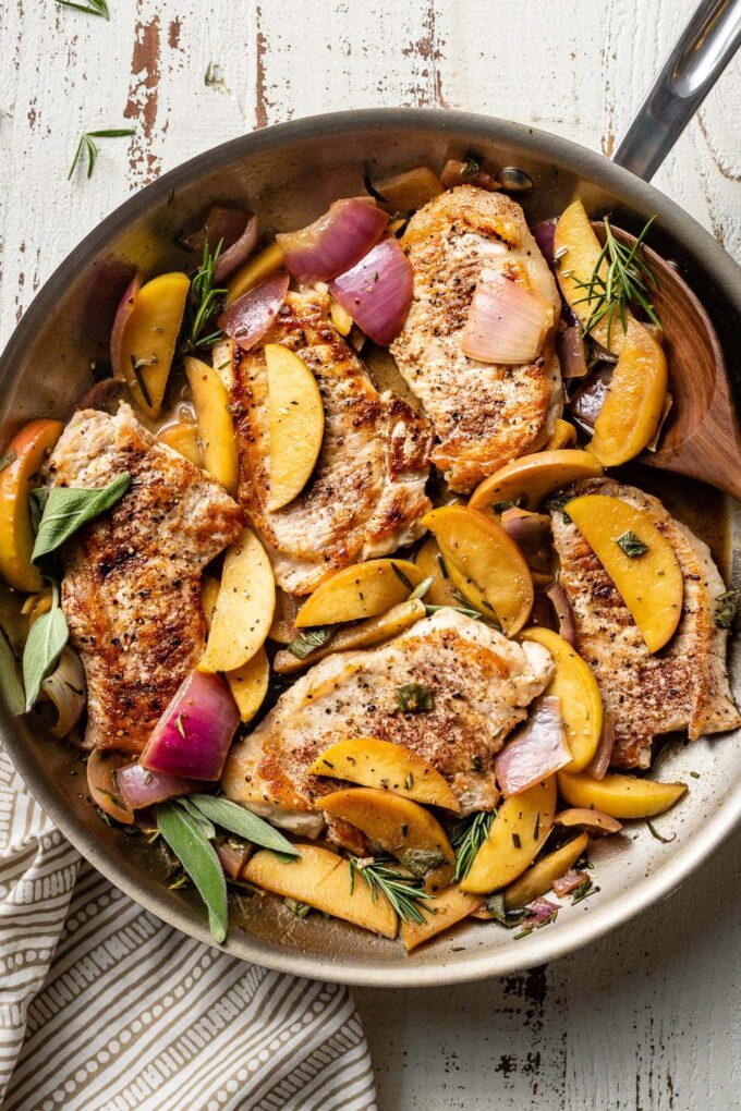 A spoon about to serve helpings of pork chops with apples and onions.