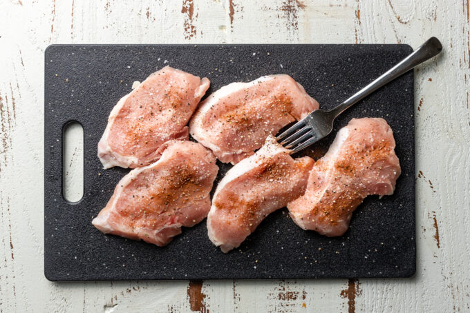 Seasoned pork chops on a plastic cutting board.