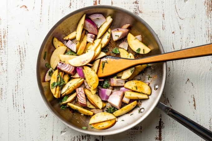 Cooked apples and onions in a skillet.