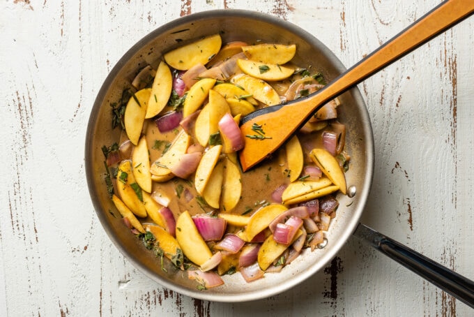 Cooked apples and onions simmering in a pan sauce.