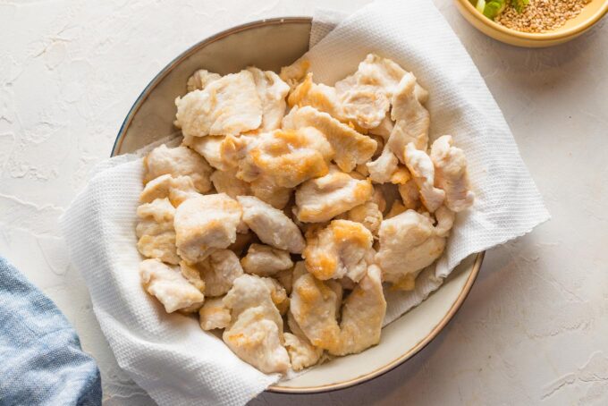 Bite-sized pieces of chicken breast cooked and set aside on a paper-towel lined plate.