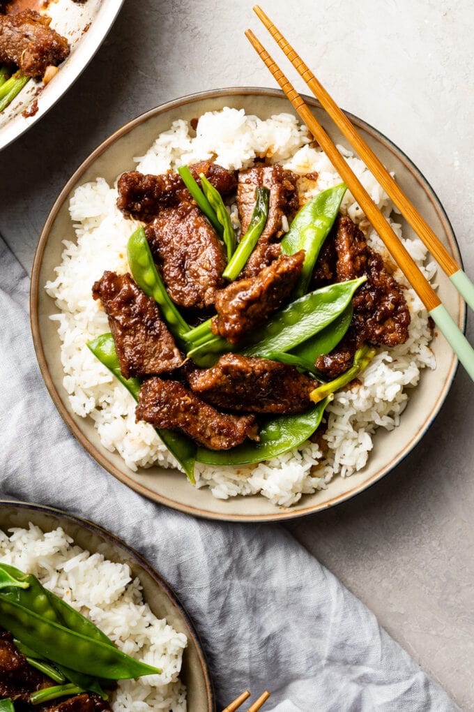 Bowls of Mongolian beef with snow peas served over white rice.