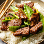 Close up of Mongolian beef with snow peas served over white rice.