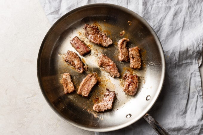 Browned pieces of flank steak in a hot skillet.