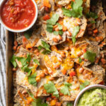 Baking sheet filled with pinto bean nachos, served with sour cream, guacamole, and salsa.