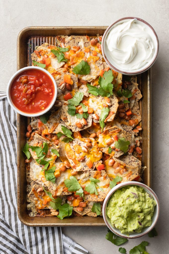 Sheet pan pinto bean nachos served with small bowls of sour cream, salsa, and guacamole.