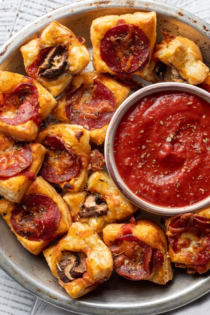 Close-up of puff pastry pizza bites with pepperoni and mushrooms served with dipping sauce.