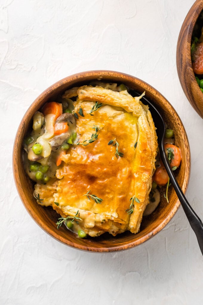 Small wooden bowl with a serving of vegetarian pot pie with a puff pastry crust.