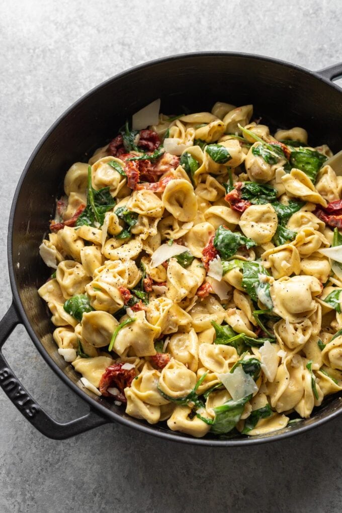 Cast iron skillet holding creamy Tuscan tortellini with spinach, sun-dried tomatoes, and shaved Parmesan.