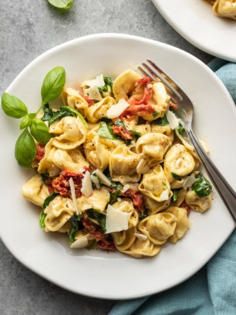 Plates of creamy Tuscan tortellini, ready to eat.