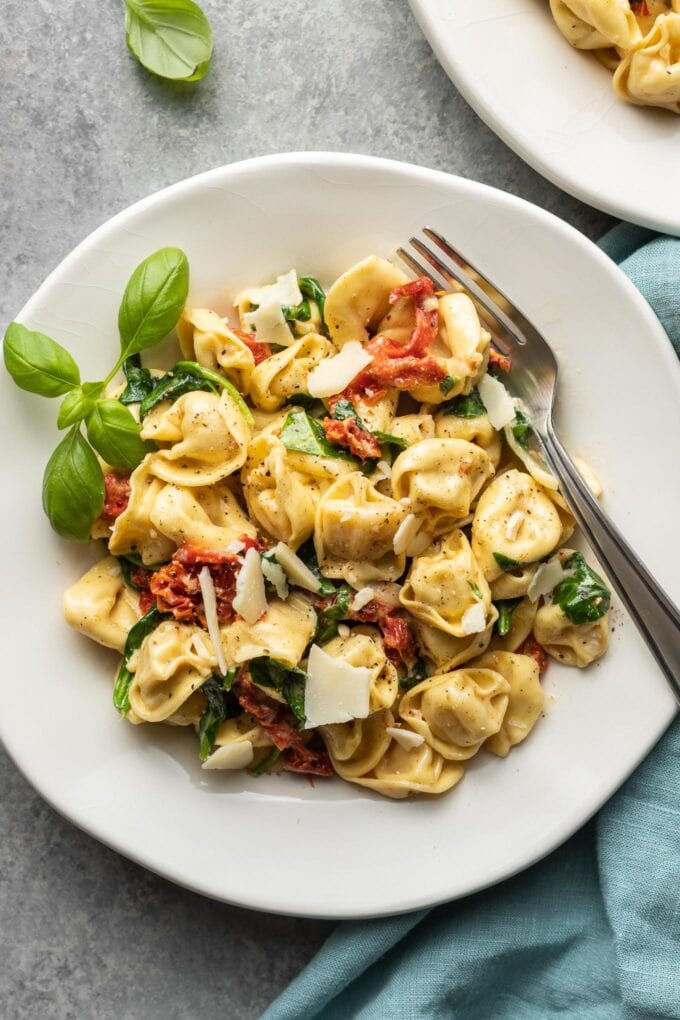 Plates of creamy Tuscan tortellini with forks and fresh basil garnish.