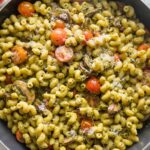 Close up overhead image of a skillet filled with pesto cavatappi with tomatoes and mushrooms.