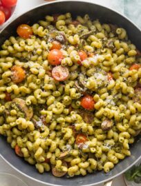 Close up overhead image of a skillet filled with pesto cavatappi with tomatoes and mushrooms.