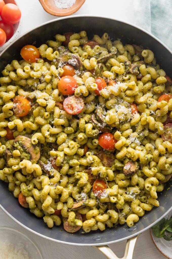 Close up overhead image of a skillet filled with pesto cavatappi with tomatoes and mushrooms.