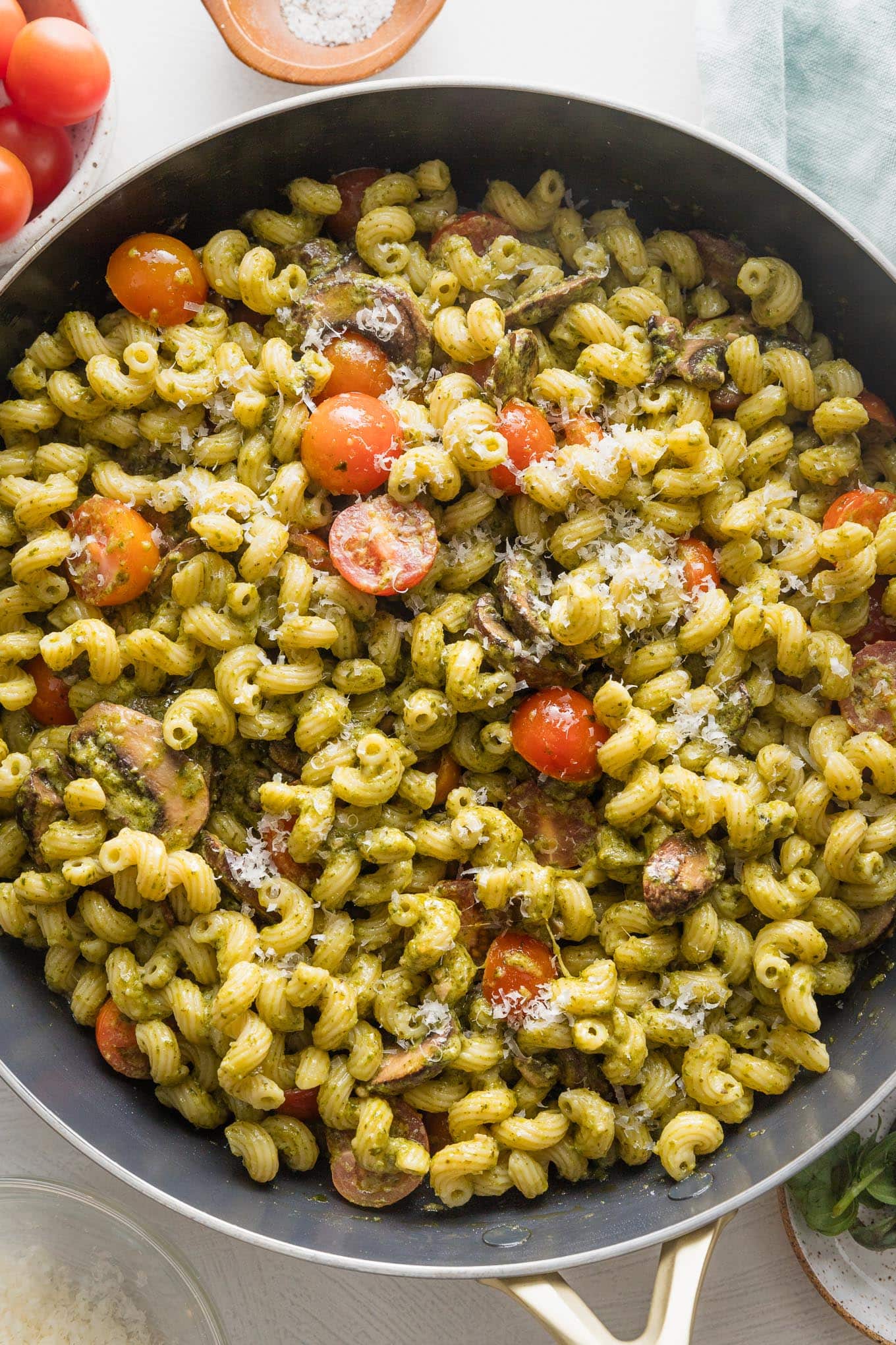 Close up overhead image of a skillet filled with pesto cavatappi with tomatoes and mushrooms.