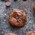 Close up of a dark chocolate cookie with chocolate chunks and sea salt sprinkled on top.