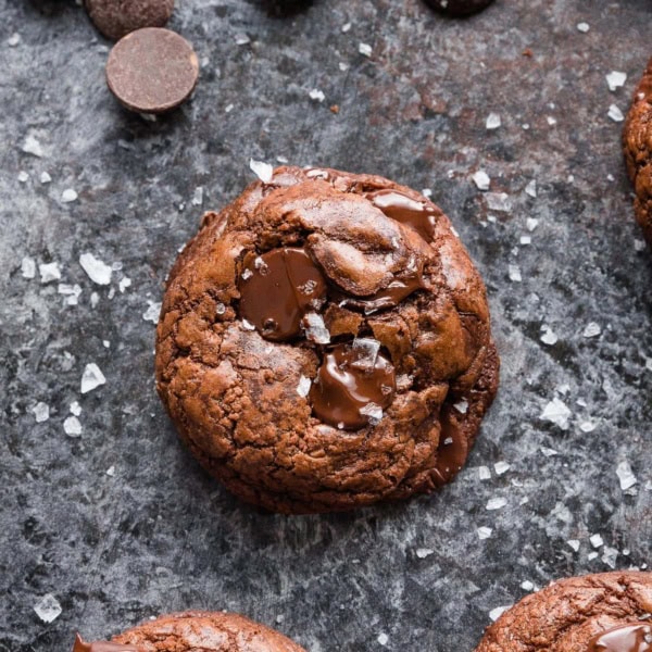 Close up of a dark chocolate cookie with chocolate chunks and sea salt sprinkled on top.