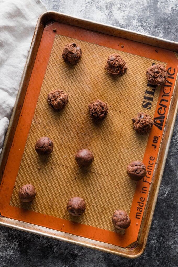 Unbaked chocolate cookie dough balls on a baking sheet.