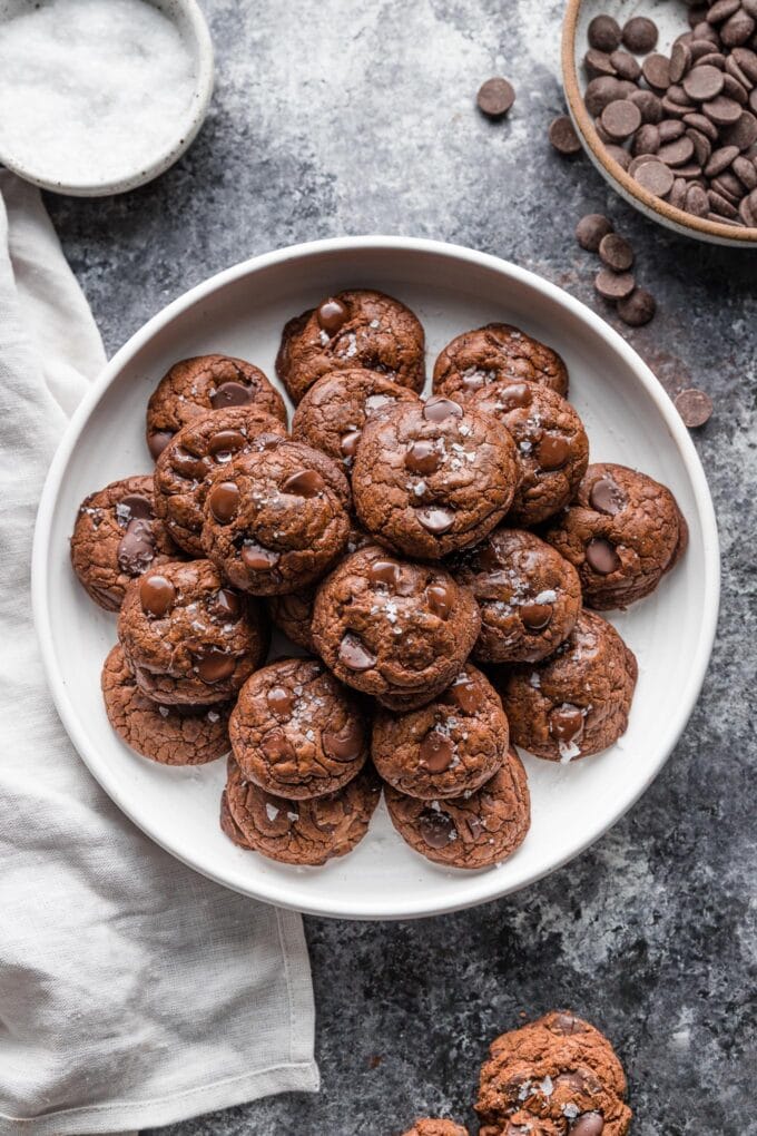Overhead image of dark chocolate cookies piled high on a white plate.