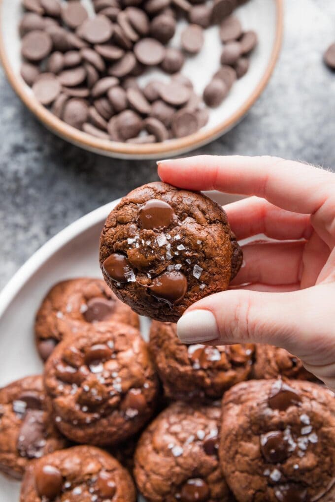 Close up of a hand holding a thick, chewy dark chocolate cookie.